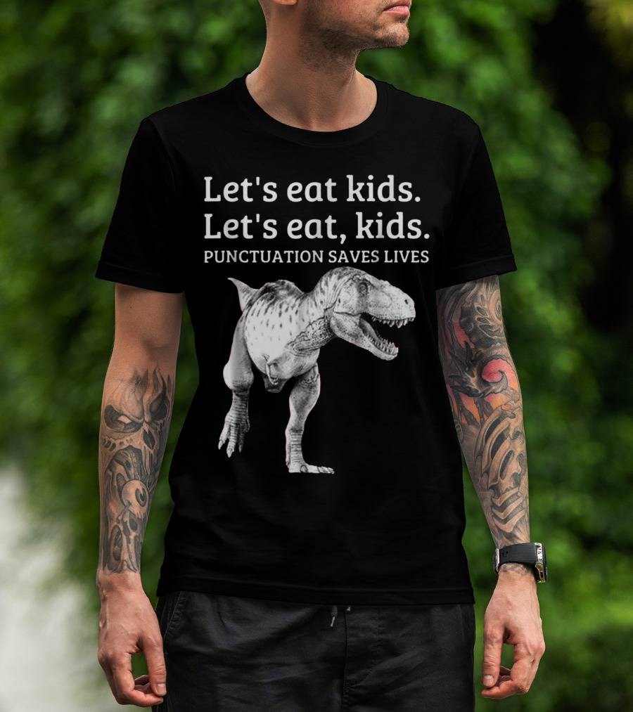 Man with tattoos models Let's Eat Kids Let's Eat Kids Punctuation Saves Lives Dinosaur T-Shirt outdoors.