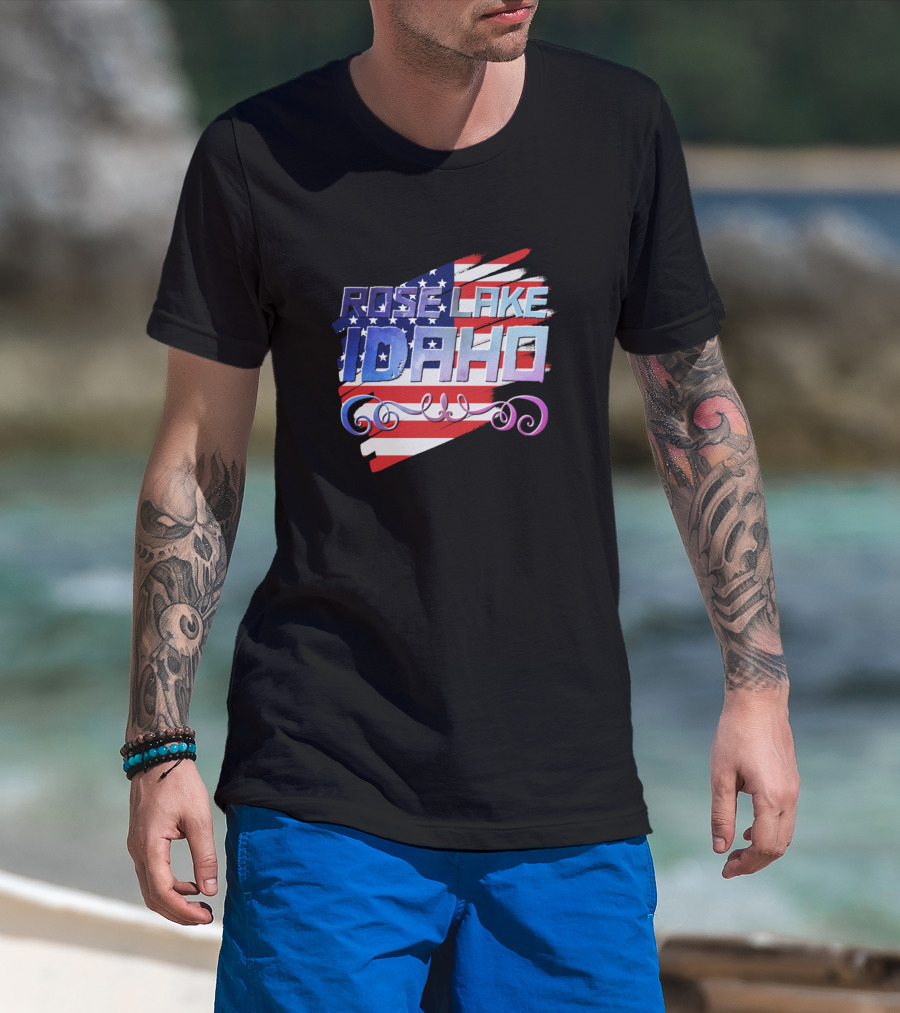 Man with tattoos models Rose Lake Idaho American Flag T-Shirt at beach.