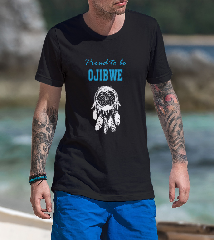 Man with tattoos models Proud to Be Ojibwe White Dreamcatcher T-Shirt at beach.