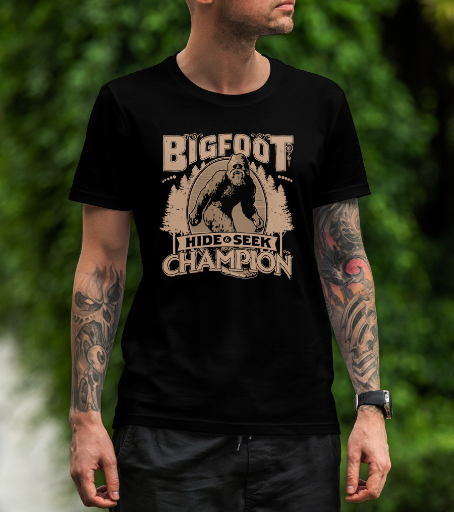 Man with tattoos models Bigfoot Hide Seek Champion T-Shirt outdoors.